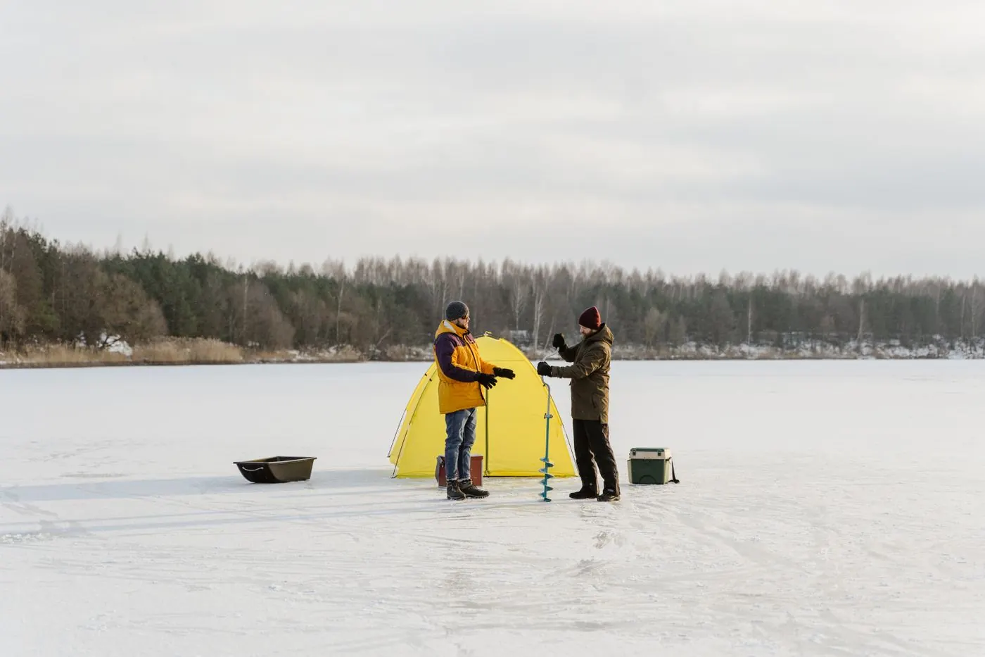 To isfiskere med isbor, utstyr og telt på et frossent vann